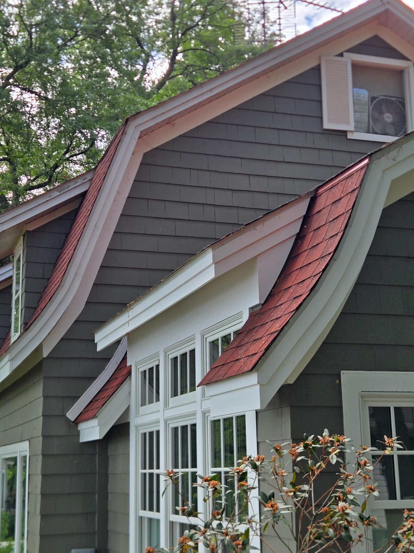 Gray house exterior with red shingled dormers