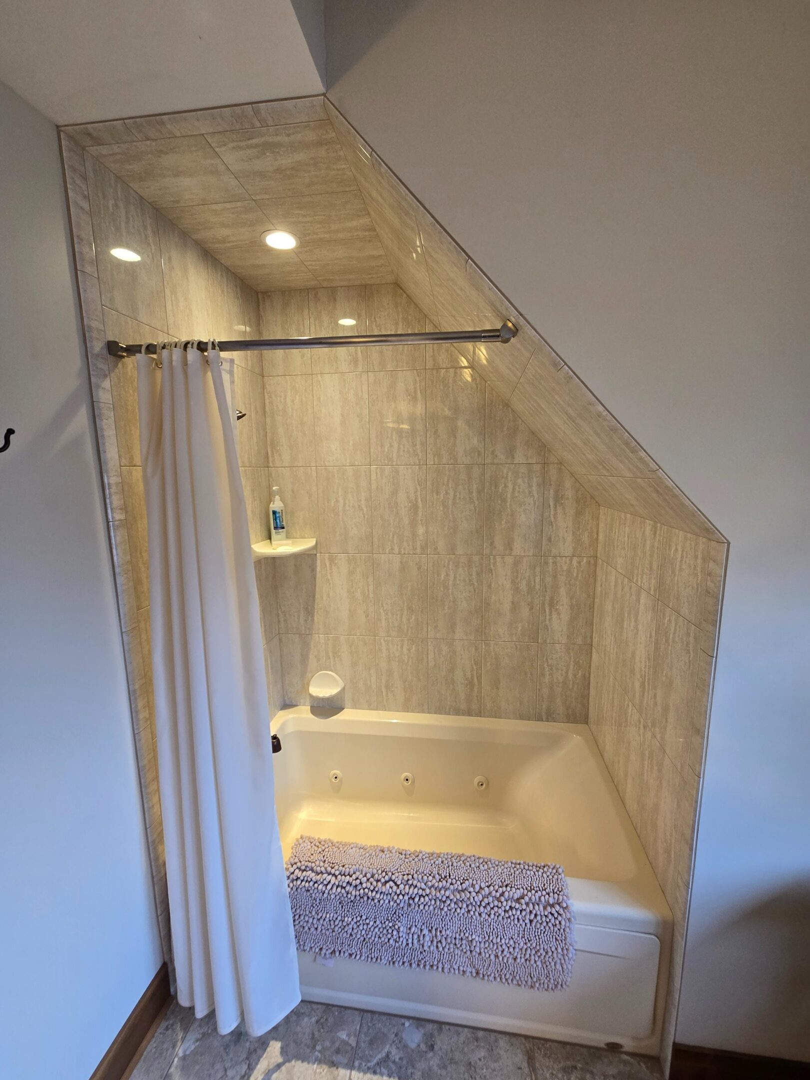 Tiled bathroom bathtub with curtain under sloped ceiling